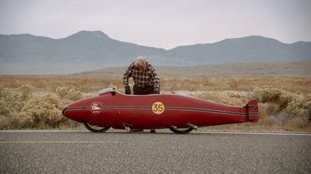 Movie still from “The World's Fastest Indian” (2005), directed by Roger Donaldson – A man sitting on the back of a red motorcycle; Wide shot, Low angle