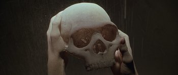 Movie still from “The X Files” (1998), directed by Rob Bowman – A person holding a skull in front of their face; Extreme Close Up shot, Overhead angle