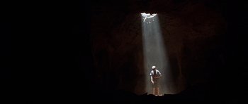 Movie still from “The X Files” (1998), directed by Rob Bowman – A man standing in a cave with light coming from the ceiling; Extreme Wide shot, Low angle