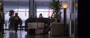Movie still from “The X Files” (1998), directed by Rob Bowman – A man sitting on a couch in an office building; Wide shot, High angle