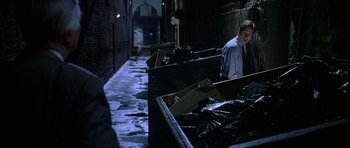 Movie still from “The X Files” (1998), directed by Rob Bowman – A man standing next to a pile of garbage; Medium shot, High angle