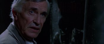 Movie still from “The X Files” (1998), directed by Rob Bowman – An older man looking at the camera in a dimly - lit room; Close Up shot, Over the shoulder angle