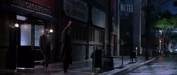 Movie still from “The X Files” (1998), directed by Rob Bowman – A man standing on the side of the street next to a piano; Wide shot, Over the shoulder angle