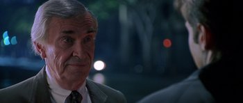 Movie still from “The X Files” (1998), directed by Rob Bowman – An older man wearing a suit and tie in front of trees; Close Up shot, Over the shoulder angle