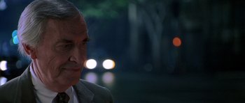 Movie still from “The X Files” (1998), directed by Rob Bowman – An older man wearing a suit standing in front of trees; Close Up shot, Over the shoulder angle