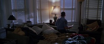 Movie still from “The X Files” (1998), directed by Rob Bowman – A police officer sitting on a couch looking out the window; Wide shot, High angle