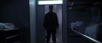 Movie still from “The X Files” (1998), directed by Rob Bowman – A soldier standing in a dark room in front of a door; Wide shot, Low angle