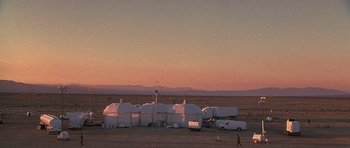 Movie still from “The X Files” (1998), directed by Rob Bowman – A man walking in front of a group of white tents; Extreme Wide shot, High angle