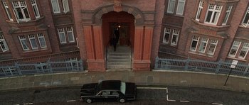 Movie still from “The X Files” (1998), directed by Rob Bowman – A car parked on the side of the road near a building; Extreme Wide shot, High angle