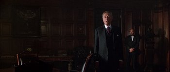 Movie still from “The X Files” (1998), directed by Rob Bowman – An older man wearing a suit and tie in a room; Medium shot, Low angle