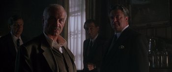 Movie still from “The X Files” (1998), directed by Rob Bowman – A group of men standing next to each other in a room; Medium shot, Low angle