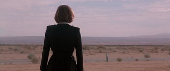 Movie still from “The X Files” (1998), directed by Rob Bowman – A woman in a black dress standing in the desert; Wide shot, Over the shoulder angle