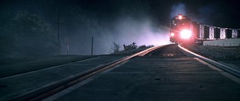 Movie still from “The X Files” (1998), directed by Rob Bowman – A train on the tracks at night with smoke billowing from it; Extreme Wide shot, Low angle