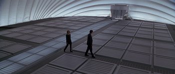 Movie still from “The X Files” (1998), directed by Rob Bowman – A man and a woman are walking in a building; Wide shot, High angle