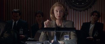Movie still from “The X Files” (1998), directed by Rob Bowman – A woman sitting in front of a camera in front of a man; Medium shot, Low angle