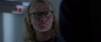 Movie still from “The X Files” (1998), directed by Rob Bowman – A man with long blonde hair wearing glasses looking at the camera; Close Up shot, Over the shoulder angle