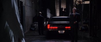 Movie still from “The X Files” (1998), directed by Rob Bowman – A man in a black suit is standing next to a black car; Wide shot, Low angle