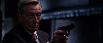 Movie still from “The X Files” (1998), directed by Rob Bowman – An older man in a suit and tie holding a gun; Close Up shot, Low angle