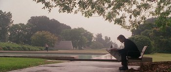 Movie still from “The X Files” (1998), directed by Rob Bowman – A person sitting on a bench under a tree; Wide shot, High angle