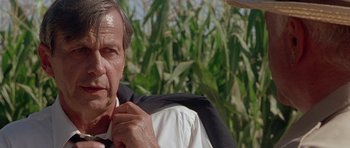 Movie still from “The X Files” (1998), directed by Rob Bowman – An older man wearing a suit and a tie in front of a field of corn; Close Up shot, Low angle
