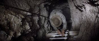 Movie still from “There Will Be Blood” (2007), directed by Paul Thomas Anderson – A man in a hat is climbing up a ladder; Wide shot, Overhead angle