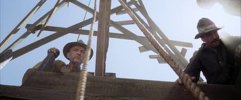 Movie still from “There Will Be Blood” (2007), directed by Paul Thomas Anderson – An old man wearing a cowboy hat standing next to a wooden structure; Medium shot, Low angle