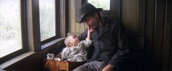 Movie still from “There Will Be Blood” (2007), directed by Paul Thomas Anderson – A man and a baby sitting next to each other; Medium shot, High angle