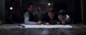 Movie still from “There Will Be Blood” (2007), directed by Paul Thomas Anderson – A group of people sitting around a wooden table; Medium shot, High angle