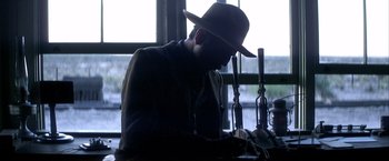 Movie still from “There Will Be Blood” (2007), directed by Paul Thomas Anderson – A man wearing a hat is sitting at a table; Medium shot, Low angle