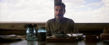 Movie still from “There Will Be Blood” (2007), directed by Paul Thomas Anderson – A man sitting at a table with a jar of coffee; Close Up shot, Over the shoulder angle