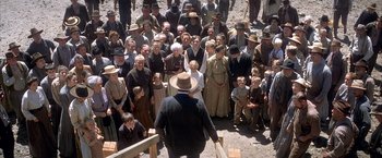 Movie still from “There Will Be Blood” (2007), directed by Paul Thomas Anderson – A group of people gathered around a man holding a bat; Wide shot, High angle
