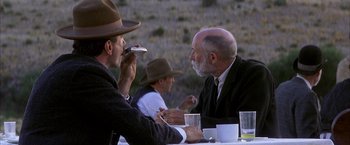 Movie still from “There Will Be Blood” (2007), directed by Paul Thomas Anderson – Two men are sitting at a table and one of them is eating a piece of cake; Medium shot, Over the shoulder angle