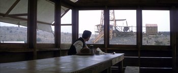 Movie still from “There Will Be Blood” (2007), directed by Paul Thomas Anderson – A man sitting at a table in front of a window; Wide shot, Over the shoulder angle