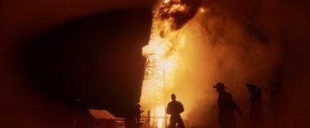 Movie still from “There Will Be Blood” (2007), directed by Paul Thomas Anderson – Two men standing in front of a burning building at night; Extreme Wide shot, Low angle