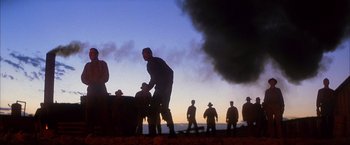 Movie still from “There Will Be Blood” (2007), directed by Paul Thomas Anderson – A group of men standing next to each other near smoke; Wide shot, Low angle