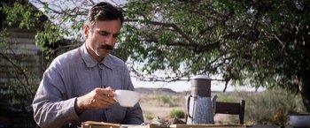 Movie still from “There Will Be Blood” (2007), directed by Paul Thomas Anderson – A man sitting at a table with a cup of coffee; Medium shot, Low angle