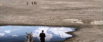 Movie still from “There Will Be Blood” (2007), directed by Paul Thomas Anderson – A man standing in front of a puddle of water; Extreme Wide shot, High angle