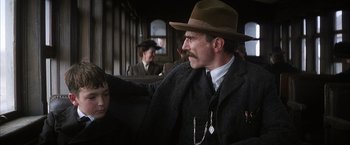Movie still from “There Will Be Blood” (2007), directed by Paul Thomas Anderson – A man with a mustache and a hat sitting on a train; Close Up shot, Over the shoulder angle