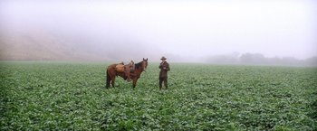 Movie still from “There Will Be Blood” (2007), directed by Paul Thomas Anderson – A man standing next to a horse in a field; Wide shot, High angle