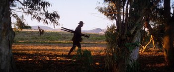 Movie still from “There Will Be Blood” (2007), directed by Paul Thomas Anderson – A man is walking through a field with two skis; Wide shot, Low angle