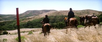 Movie still from “There Will Be Blood” (2007), directed by Paul Thomas Anderson – Two people riding horses through a field of tall grass; Extreme Wide shot, Low angle