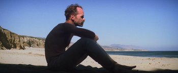 Movie still from “There Will Be Blood” (2007), directed by Paul Thomas Anderson – A man sitting on the beach with a surfboard; Medium shot, Low angle