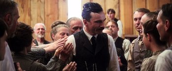 Movie still from “There Will Be Blood” (2007), directed by Paul Thomas Anderson – A group of people clapping around a man in a vest; Medium shot, Low angle