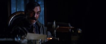 Movie still from “There Will Be Blood” (2007), directed by Paul Thomas Anderson – A man sitting at a table in a dark room; Close Up shot, Over the shoulder angle
