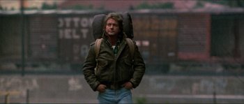 Movie still from “They Live” (1988), directed by John Carpenter – A man in a jacket with a backpack on his back; Medium shot, Low angle