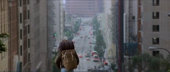 Movie still from “They Live” (1988), directed by John Carpenter – A person with a backpack walking down a street; Wide shot, Low angle