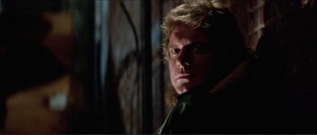 Movie still from “They Live” (1988), directed by John Carpenter – A person wearing a black shirt; Close Up shot, Low angle