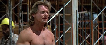 Movie still from “They Live” (1988), directed by John Carpenter – A man with long blond hair and no shirt; Close Up shot, Low angle