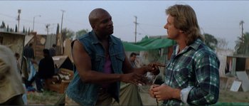 Movie still from “They Live” (1988), directed by John Carpenter – Two men talking to each other outside in the day; Medium shot, Over the shoulder angle