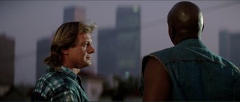 Movie still from “They Live” (1988), directed by John Carpenter – A man standing next to another man on a city street; Close Up shot, Over the shoulder angle